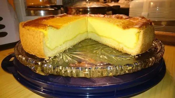 Ein Käsekuchen liegt auf einem runden Teller, halbiert, mit einer goldbraunen Oberfläche und cremigem, hellgelbem Inneren.
