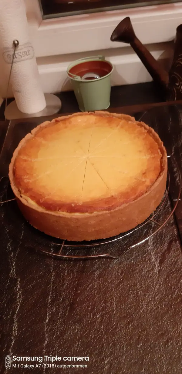 Ein perfekt gebackener Käsekuchen steht auf einem klassischen schwarzen Marmortisch, mit einem Stück, das bereits angeschnitten ist.