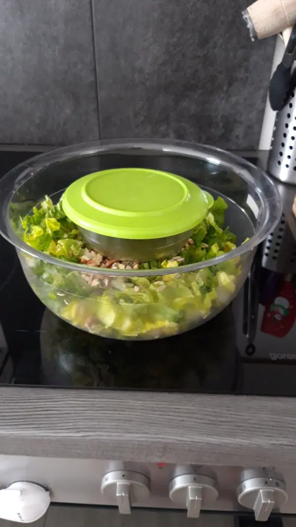 Ein transparentes Glas mit frischem Salat und einem grünen Deckel steht auf einem Herd, bereit zum sicheren Transport.