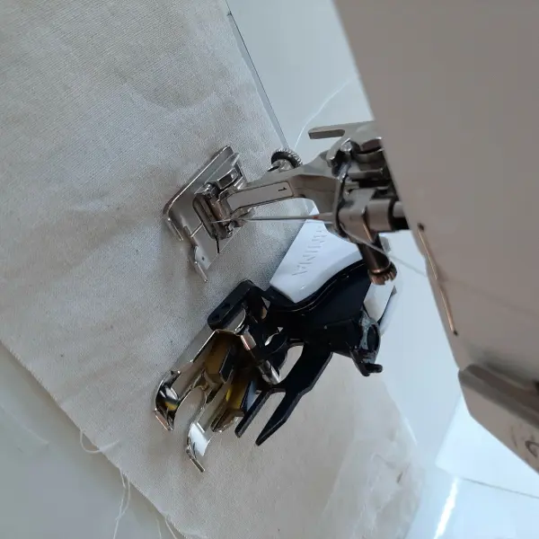 Eine Nähmaschine benutzt einen Nähfuß, um Stoff für ein Babynest zu nähen. Der Arbeitsbereich ist hell und sauber.