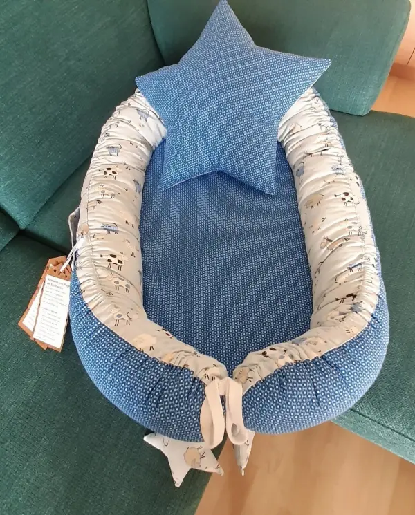 Ein Babynest in sanftem Blau mit einem passenden, sternförmigen Kissen liegt gemütlich auf einem grünen Sofa.