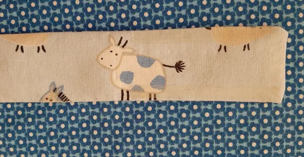 Ein gestickter Baumwollstoff mit Kühen liegt auf einem blauen Untergrund und zeigt niedliche Tiermuster für Babynester.