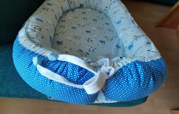 Ein Babynest in blauen Stoffen liegt auf einem grünen Sofa, bereit für ein Baby zum Nappen oder Entspannen.