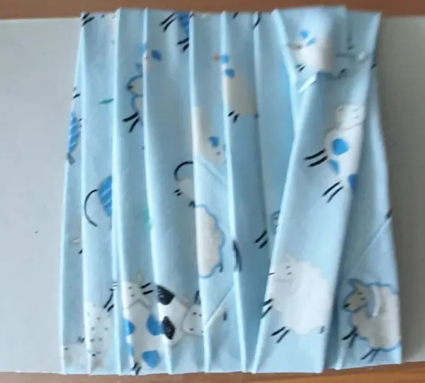Ein gestreiftes Babynest aus hellblauem Stoff mit Schafmotiven liegt auf einer flachen Oberfläche und wartet auf die Fertigstellung.