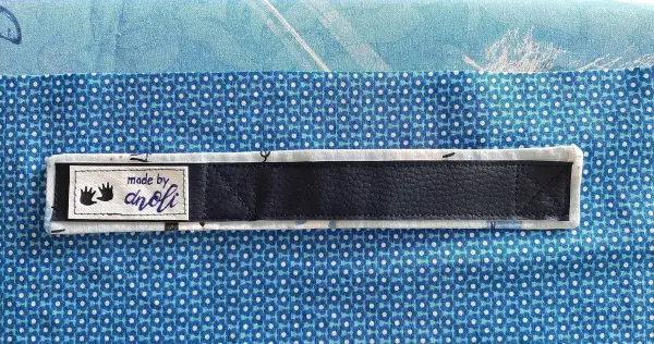 Ein schwarzes Namensetikett mit "made by" auf einem blauen Stoff, der für das Nähen eines Babynests verwendet wird.