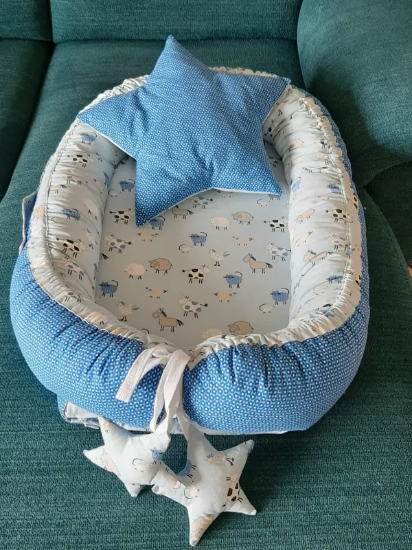 Ein Babynest in sanften Blautönen liegt auf einem grünen Sofa, dekoriert mit einem Sternkissen und kleinen Stoffsternen.