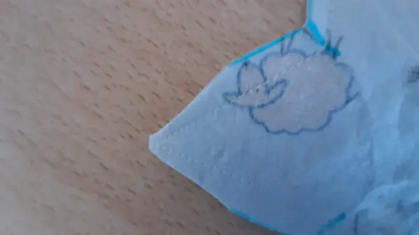 Ein süßes Babynest aus blauem Stoff mit einem gemalten Schafmotiv liegt auf einem Holzuntergrund, umgeben von Nähmaterialien.