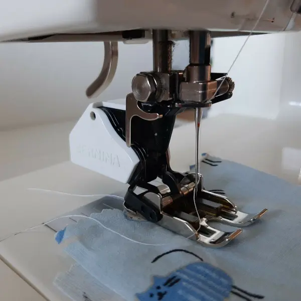 Eine Nähmaschine näht einen Stoff mit blauen Motiven, ideal für das Babynest. Die Nahteinstellungen sind präzise.