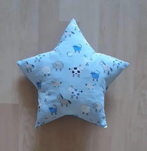 Ein sternföriges Kissen aus hellblauem Stoff, das auf einem Holzfußboden liegt, zeigt Tiermuster, ideal für ein Babynest.