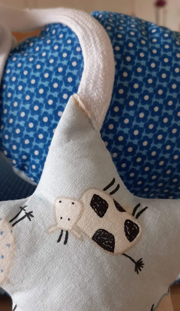 Ein Babynest mit blauer, gepunkteter Oberfläche und einem Stern mit Kuhmotiv, ideal für eine gemütliche Babyzeit.