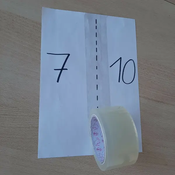 Eine Papierunterlage zeigt die Zahlen 7 und 10, während ein Klebeband entlang eines gestrichenen Schnitts positioniert ist.