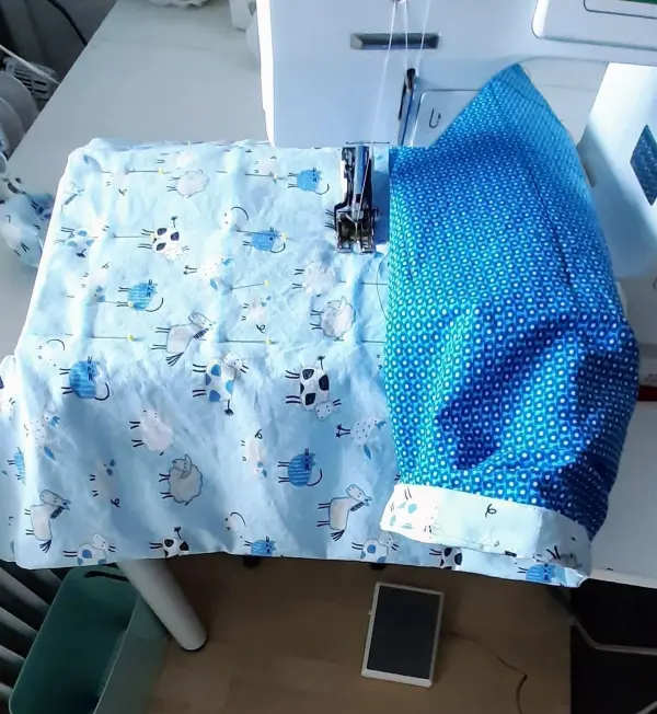 Auf einem Nähtisch liegt ein babynest-fertiges Stück in bunten Stoffen, während eine Nähmaschine bereit für den nächsten Stich ist.