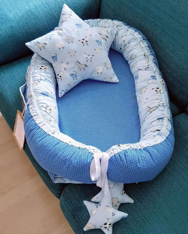 Ein Babynest aus blauer Stoffe mit einem Kissen liegt bequem auf einer grünen Couch und strahlt eine gemütliche Atmosphäre aus.