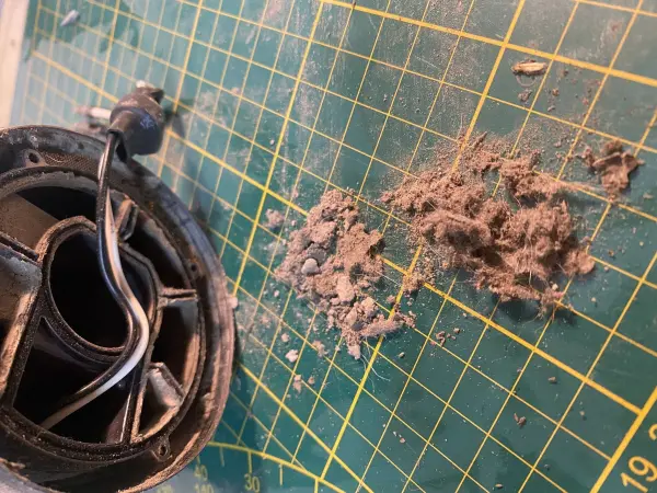 Ein Dyson Staubsauger liegt auf einem grünen Schneidebrett, daneben ist Staub und Schmutz verstreut.