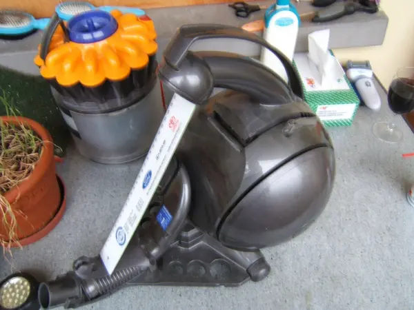 Ein Dyson Staubsauger liegt auf einem Boden, umgeben von verschiedenen Haushaltsgegenständen und Pflanzen.