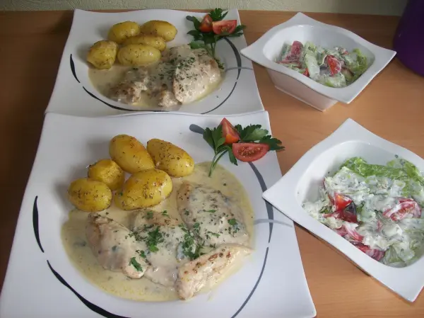 Hähnchen-Schnitzel in Gorgonzola-Soße liegt auf Tellern, umgeben von kleinen Kartoffeln und einem frischen Salat.
