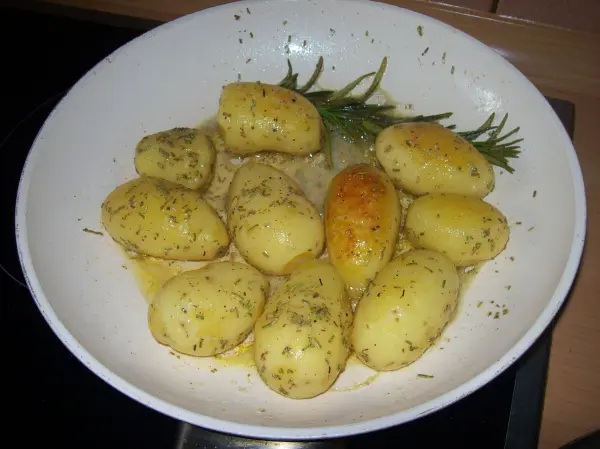 Zarte, gekochte Kartoffeln liegen in einer weißen Schüssel, umgeben von Kräutern, bereit zum Servieren mit Hähnchen-Schnitzel.