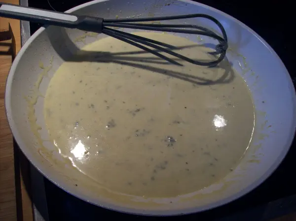 Eine cremige Gorgonzola-Soße wird in einer Pfanne mit einem Schneebesen glatt gerührt, um das Hähnchen-Schnitzel zu verfeinern.