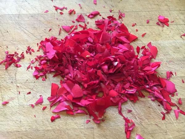 Rote Rosenblätter liegen zerkleinert auf einem Holzbrett, bereit für die Zubereitung von Duftrosen-Gelee ohne Alkohol.