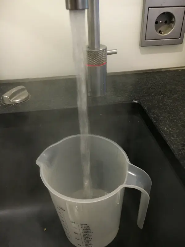 Ein Messbecher wird mit heißem Wasser gefüllt, während er in einer modernen Küche auf der Arbeitsfläche steht.