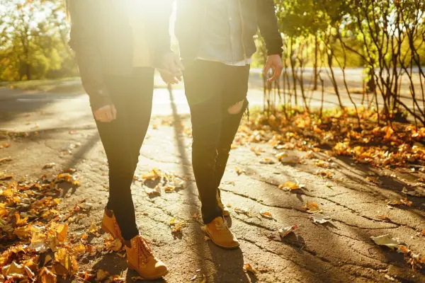 Zwei Personen gehen einen sonnigen Weg entlang, umgeben von bunten Herbstblättern, die das Outdoor-Erlebnis genießen.