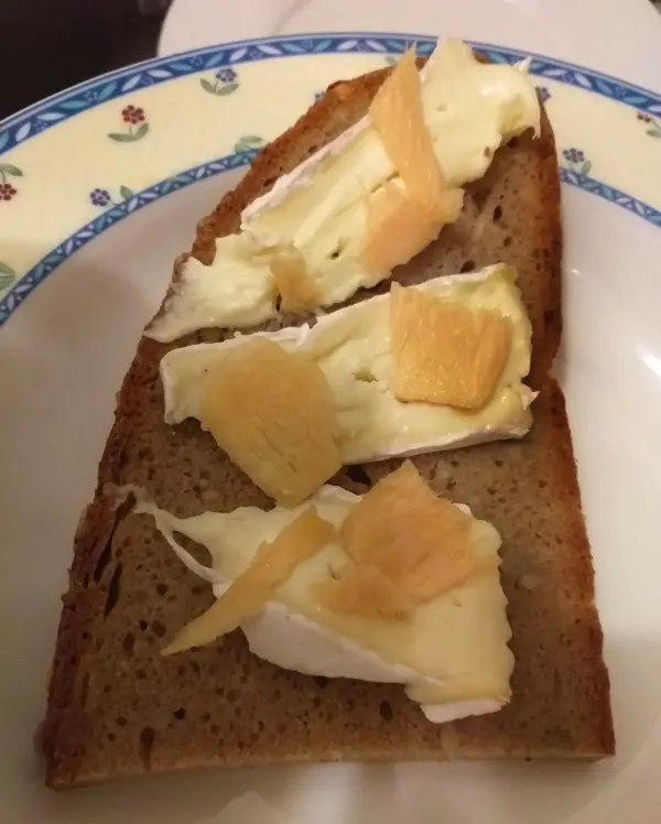 Eine Scheibe Vollkornbrot ist mit cremigem Käse und mildem, eingelegtem Ingwer belegt, serviert auf traditionellem Porzellanteller.
