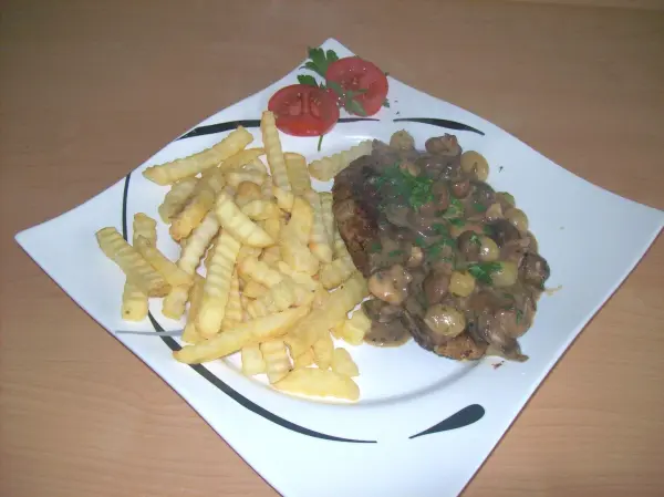 Ein krosses Winzer-Kotelett liegt auf einem Teller, garniert mit einer Pilzsauce, daneben liegen knusprige Pommes.