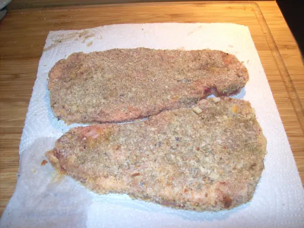 Zwei panierte Koteletts liegen auf einem Küchenpapier, bereit zum Braten in einer geselligen Kochumgebung.
