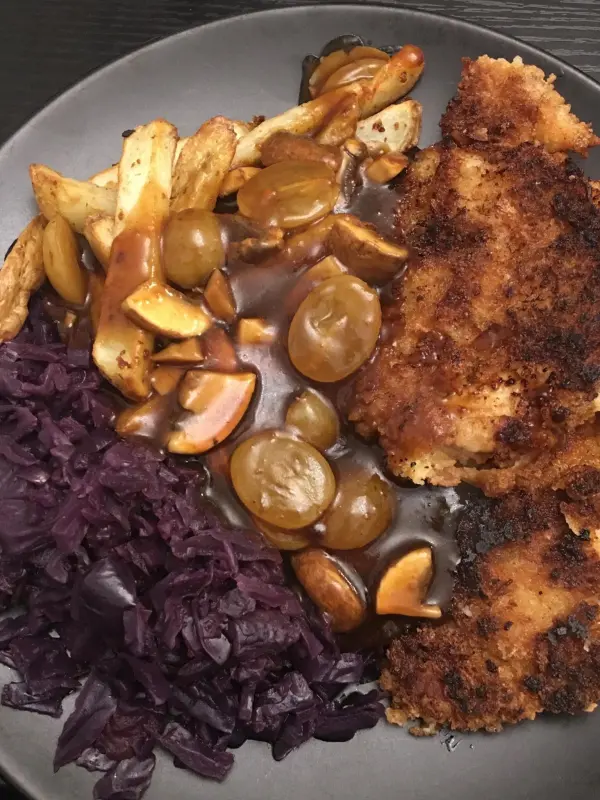 Koteletts auf einem Teller liegen neben lila Kraut und einer Sauce mit Äpfeln, in einem modernen Essumfeld arrangiert.
