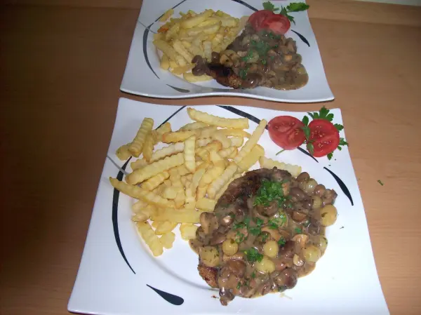 Saftige Winzer-Koteletts liegen auf Tellern neben knusprigen Pommes, umgeben von frischen Tomaten und Kräutern.