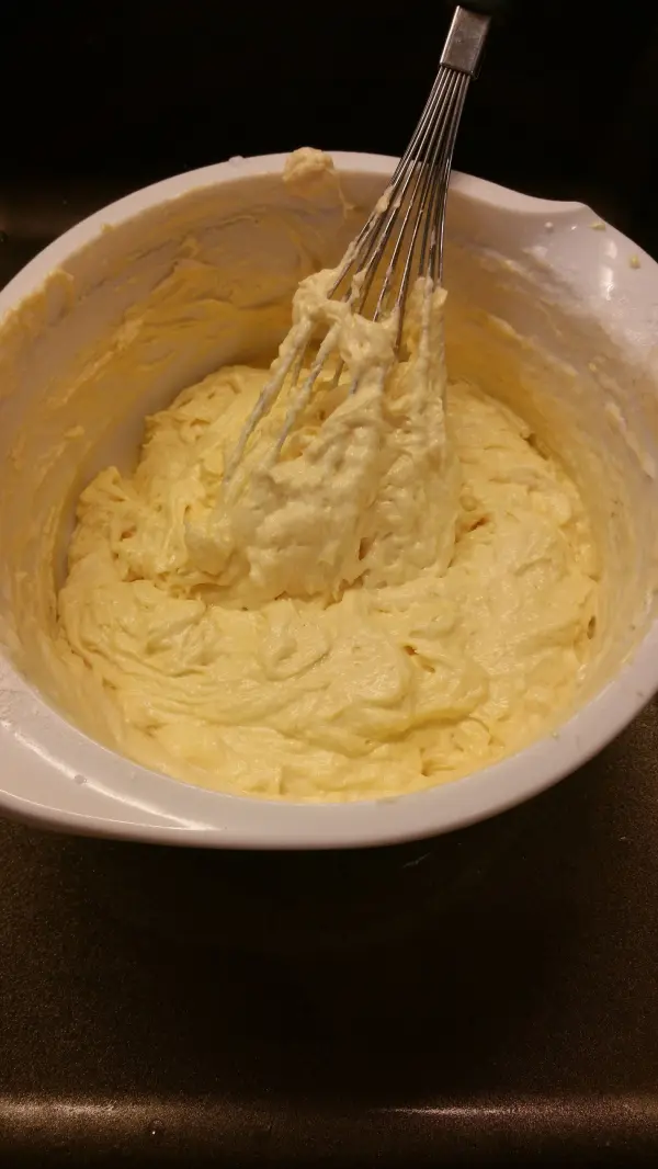 Der Quark-Gugelhupf-Teig wird mit einem Schneebesen in einer weißen Schüssel gerührt, um eine gleichmäßige Konsistenz zu erreichen.
