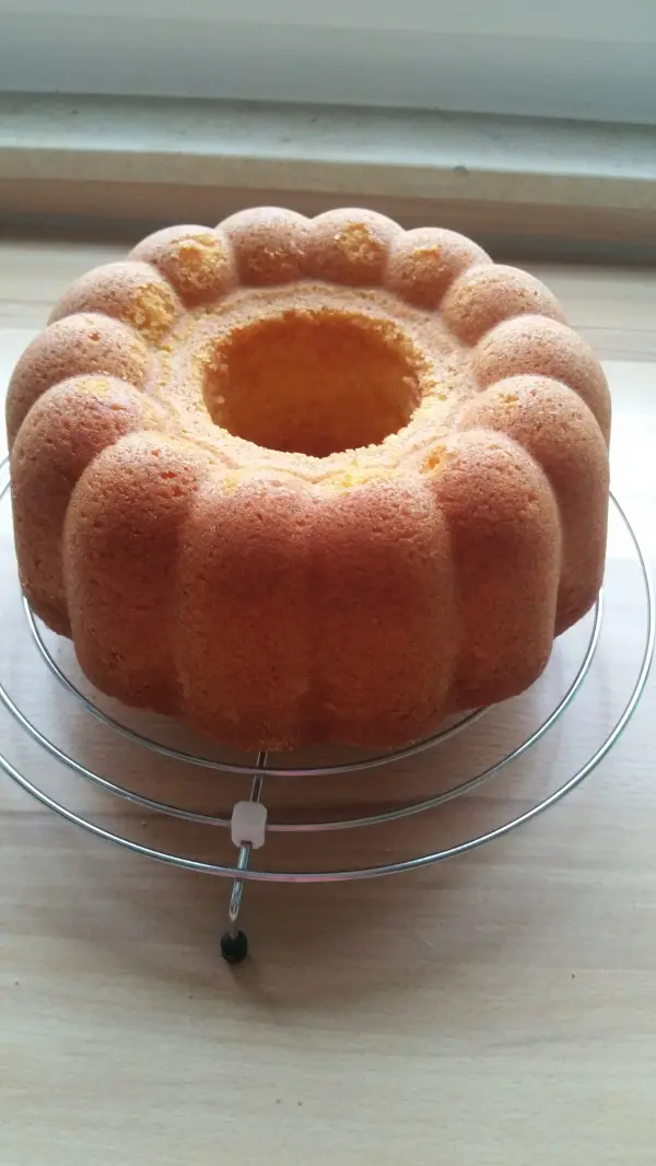 Ein goldbrauner Quark-Gugelhupf steht auf einem Bakeständer und zeigt seine glatte, runde Form in natürlichem Licht.