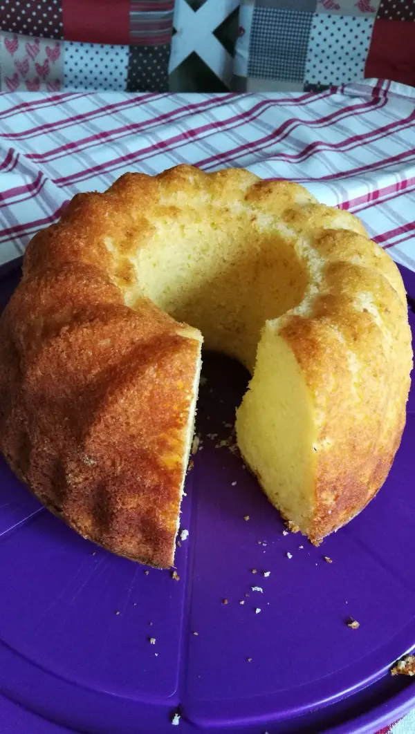 Ein Gugelhupf aus Quark steht auf einem lila Teller, mit einer Schnittkante sichtbar, umgeben von kariertem Tischdecken.