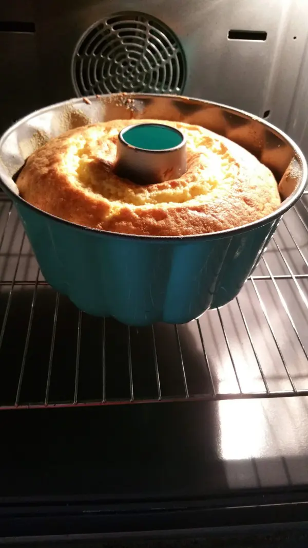 Ein hoher, goldbrauner Quark-Gugelhupf backt in einer blauen Form im Ofen und verbreitet einen appetitlichen Duft.