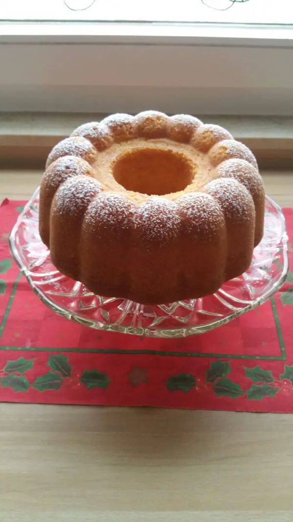 Ein Quark-Gugelhupf steht auf einem Glasständer, umgeben von einer festlichen roten Unterlage, mit Puderzucker bestäubt.