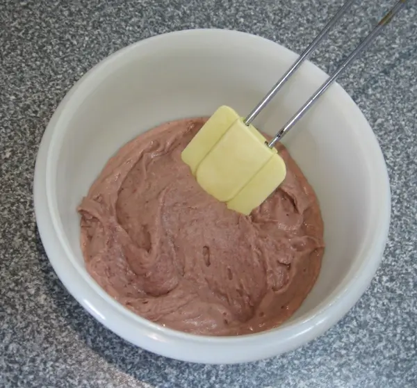 Eine Schüssel mit einer cremigen, linsenbasierten Frikadellenmasse, die mit einem Spatel gerührt wird, steht auf einer Arbeitsfläche.