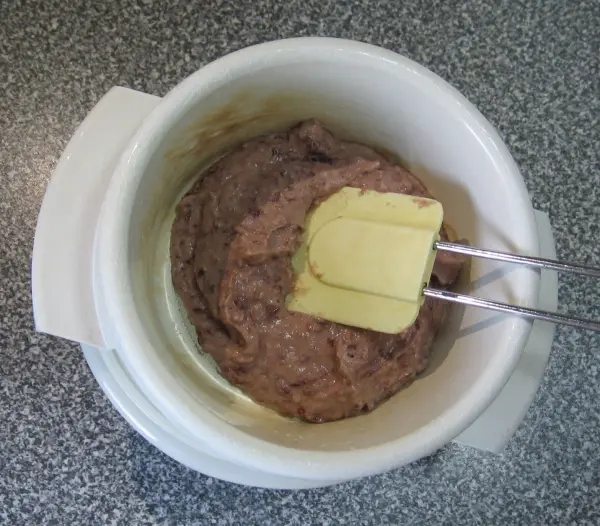 Eine cremige Frikadellenmasse mit Linsen wird mit einem Mixer in einer Schüssel zubereitet, auf einer grauen Arbeitsfläche.
