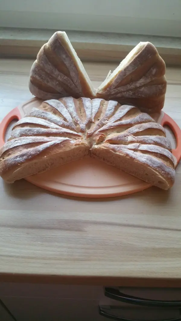 Ein Brötchen-Kranz liegt auf einem Teller, präsentiert mit aufgeschnittenen Stückchen, die dekorativ angeordnet sind.