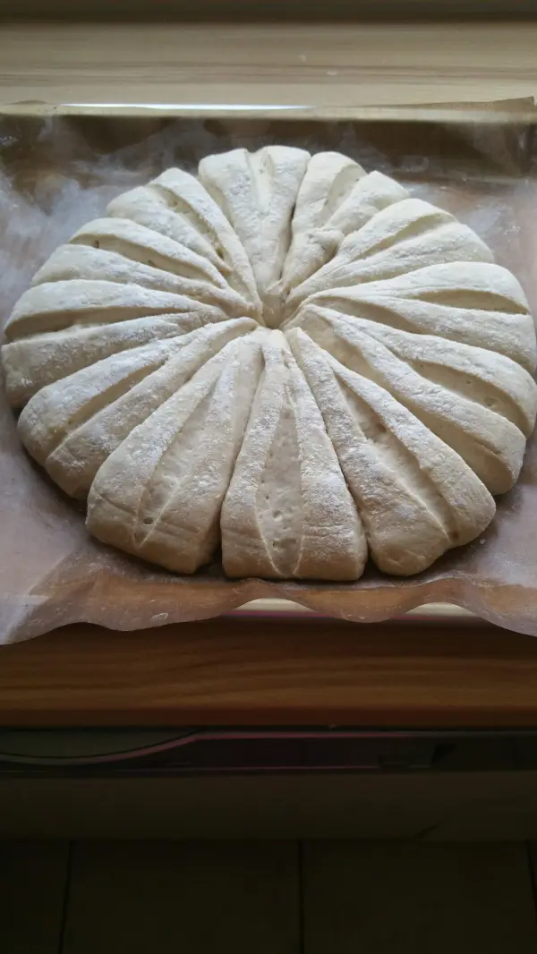 Ein rohrförmiger Brötchen-Kranz aus rohem Teig liegt auf einem Backblech, bereit zum Backen in einer hellen Küche.