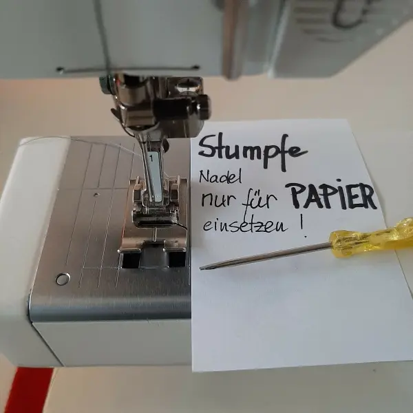 Eine Nähmaschine mit einer Zettelnotiz daneben, die erklärt, dass die Nadel nur für Papier verwendet werden soll.