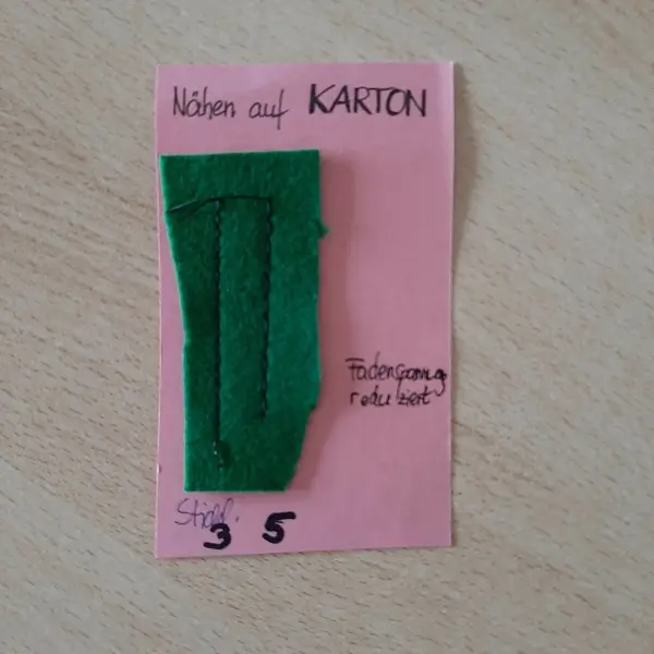Eine grüne Filz-Applikation ist auf einer rosa Karte befestigt, die den Prozess des Bastelns im weihnachtlichen Kontext zeigt.