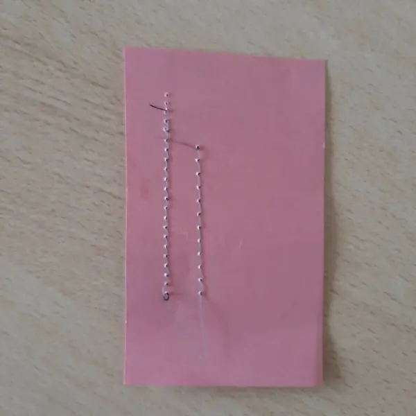 Eine pinkfarbene Karte liegt auf einem Tisch, auf der zwei silberne Fäden befestigt sind, die Wunsch-Erfüllung symbolisieren.