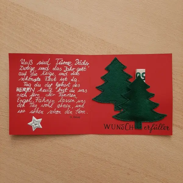 Eine rote Karte mit zwei grünen Tannenbäumen darin, die eine persönliche Weihnachtsnachricht enthält.
