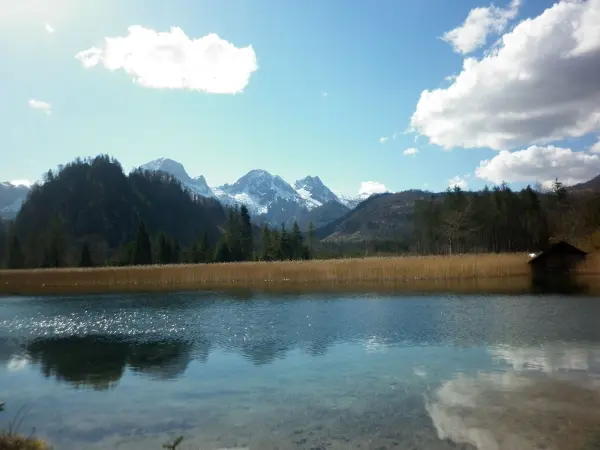 Ein ruhiger See spiegelt die umliegenden Berge und den blauen Himmel wider, umgeben von der friedlichen Natur.