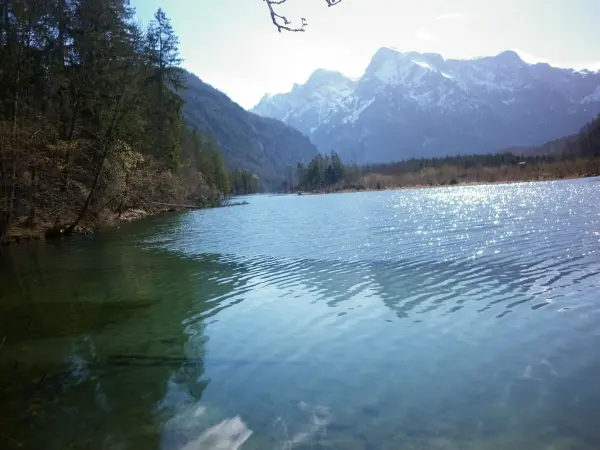 Ein klarer See spiegelt die Sonne wider, umgeben von majestätischen Bergen und dichten Wäldern. Ein perfekter Ort, um die Natur zu genießen.