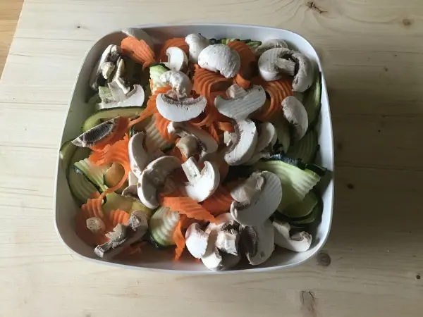 Ein schalenförmiges Gericht mit farbenfrohem Gemüse wie Zucchini, Karotten und Champignons, bereit für die Zubereitung.