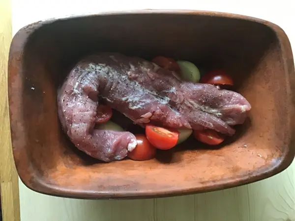 Ein Schweinefilet liegt auf einer Unterlage aus Tomaten, bereit zum Kochen für ein Gemüse-Nudel-Gericht.