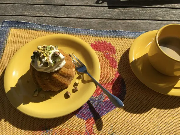 Ein saftiger Karottenkuchen liegt auf einem gelben Teller, dekoriert mit Sahne und Nüssen, neben einer Tasse Kaffee.