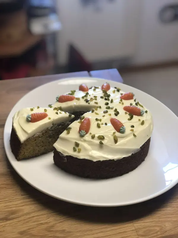 Ein saftiger Karottenkuchen auf einem weißen Teller, mit frischer Sahne und Dekoration, steht in einer modernen Küche.