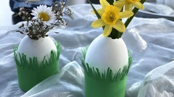 Zwei kreativ gestaltete Eierväschen aus weißen Eiern mit Blumenarrangements stehen in einem festlichen, hellen Umfeld.